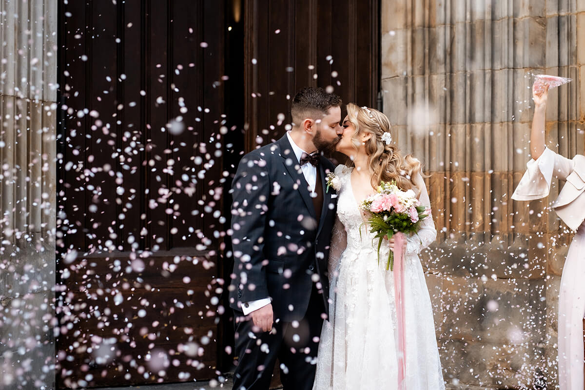 fotograf ślubny Wrocław - para młoda wychodzi z kościoła, są szczęśliwi, a w powietrzu wiruje kolorowe confetti
